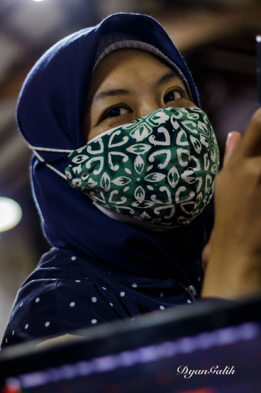 A young woman wearing a blue dark hijab and green motif mask.